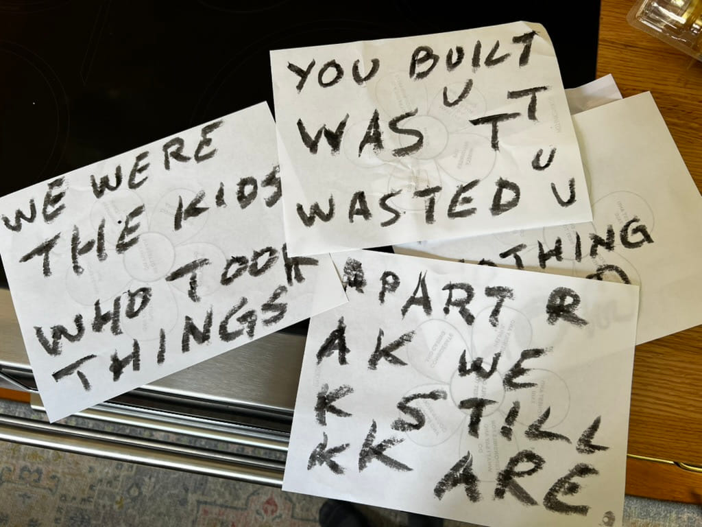 Sheets of paper hand-lettered in black paint stick, piled on a kitchen counter